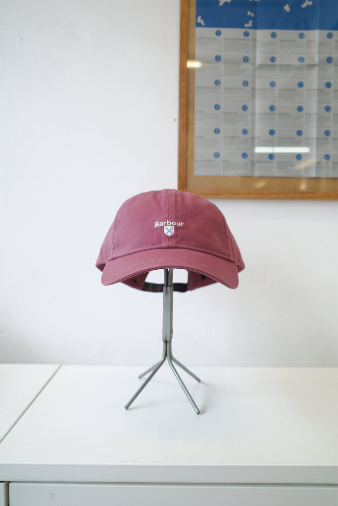 A dusty rose pink baseball cap with a white embroidered logo reading 'Bloom' and a small flower icon, displayed on a silver metal stand on a white table.