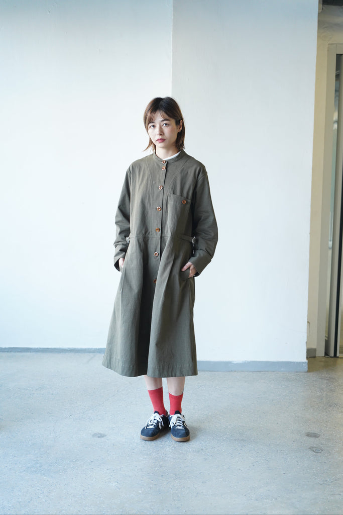  a long-sleeved, knee-length olive green utility dress with brown buttons, paired with red socks and navy sneakers.