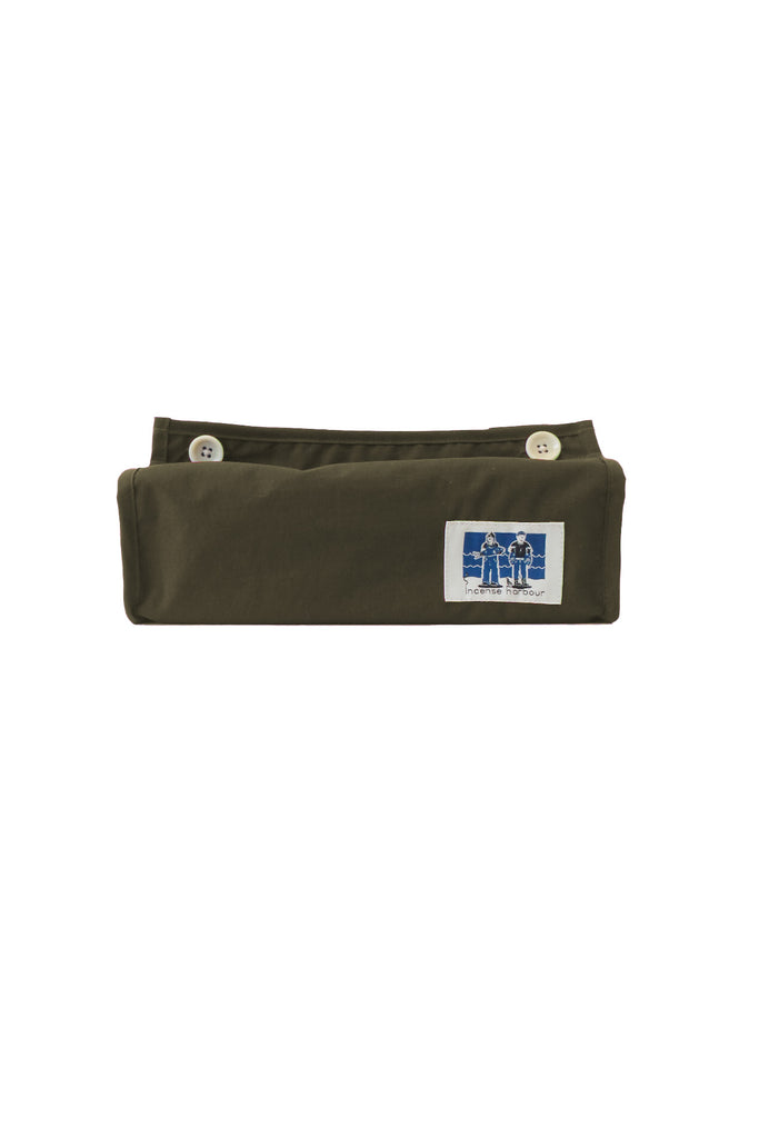 A folded grey green fabric accessory, likely a belt or strap, featuring a small white rectangular patch with a blue graphic and two gold-tone snap buttons near the top edge, shown against a plain white background.