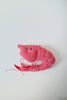 A pink knitted shrimp plush toy with embroidered eyes and mouth, lying on a plain white surface.